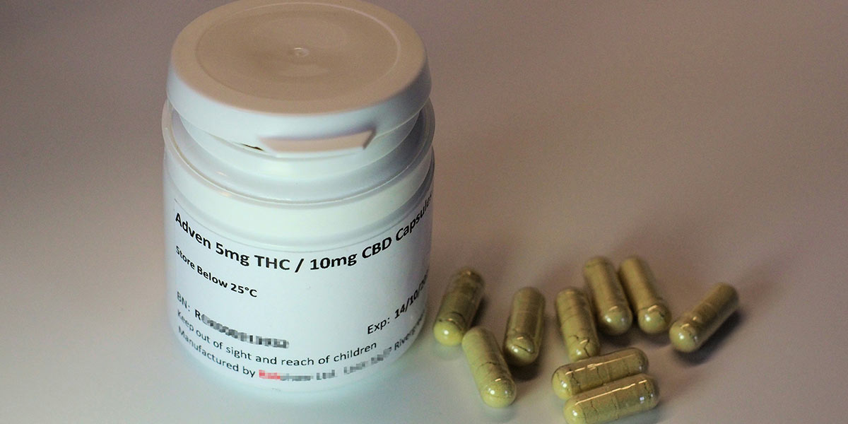 Medizinisches Döschen mit CBD-Kapseln, daneben liegen mehrere der Kapseln.